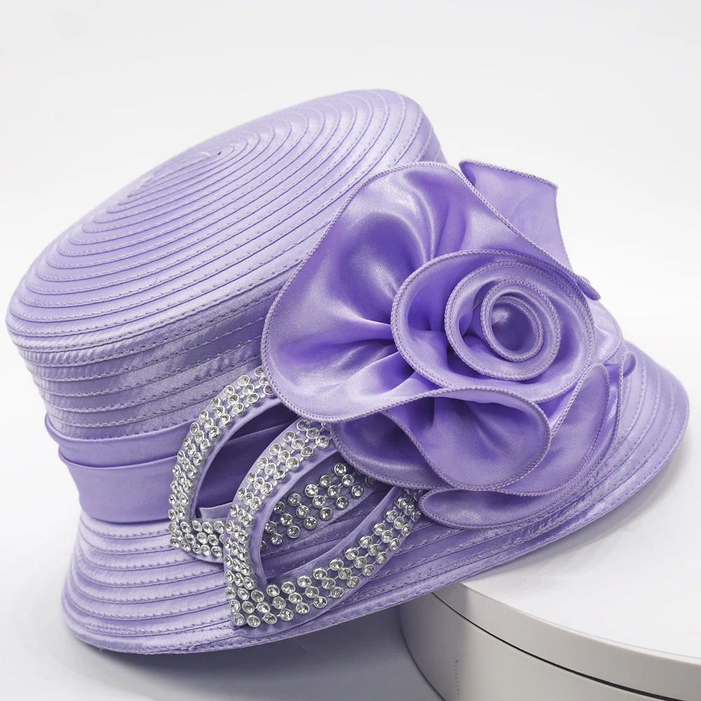 Side view of a lavender church hat featuring satin floral detailing and double-loop rhinestone accents, displayed on a white stand.