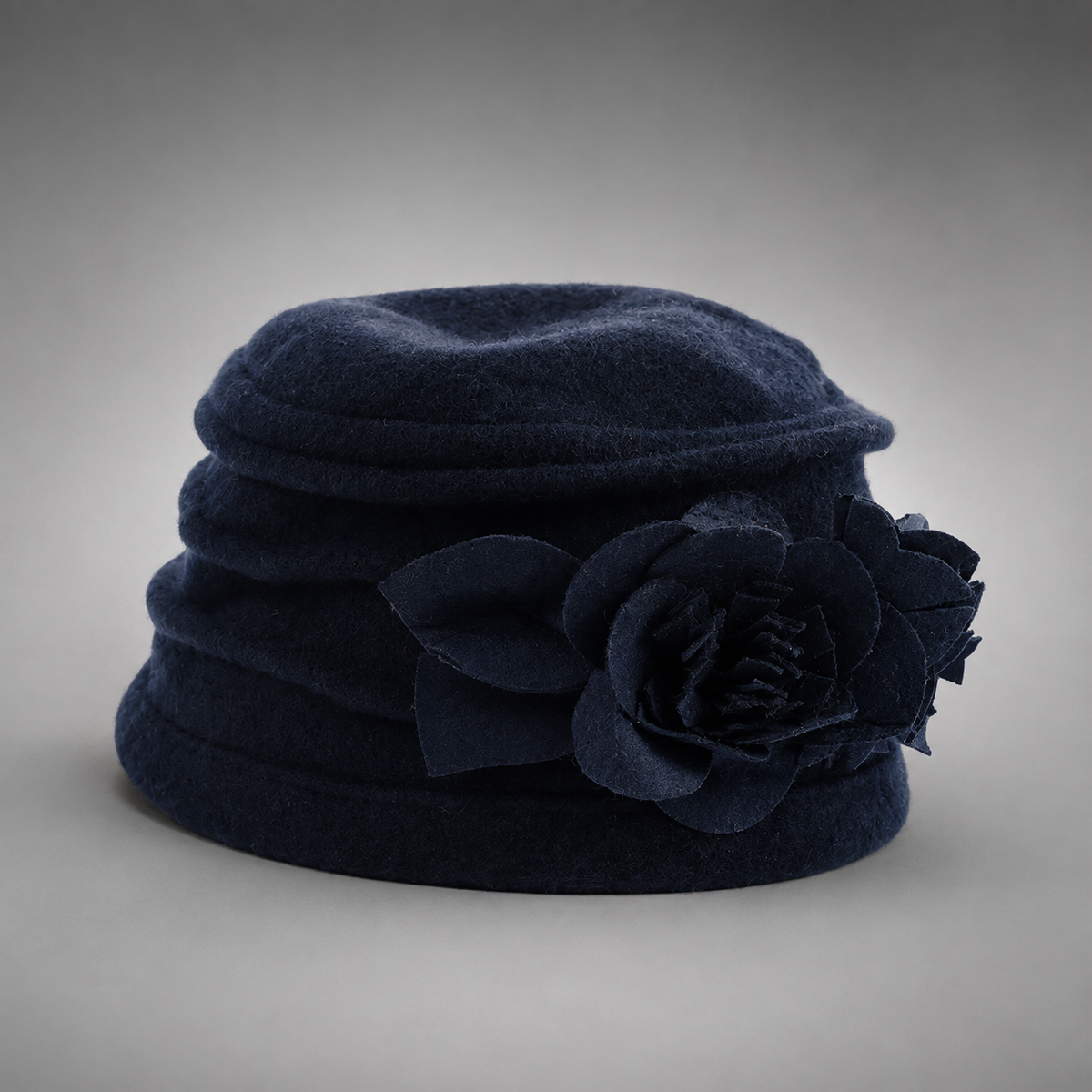 A dark navy blue felt hat featuring a large matching fabric flower decoration on the side, photographed against a neutral gray gradient background.