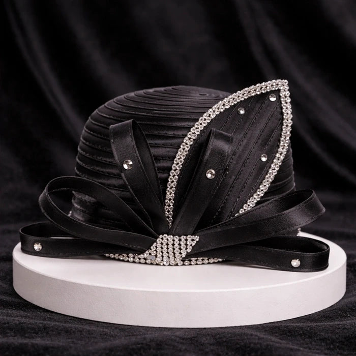 Classic black satin church hat with rhinestone accents and satin ribbon detailing, displayed on a white base with a black velvet backdrop for a refined look.