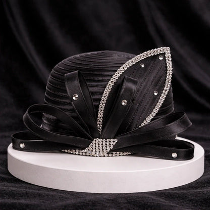 Classic black satin church hat with rhinestone accents and satin ribbon detailing, displayed on a white base with a black velvet backdrop for a refined look.