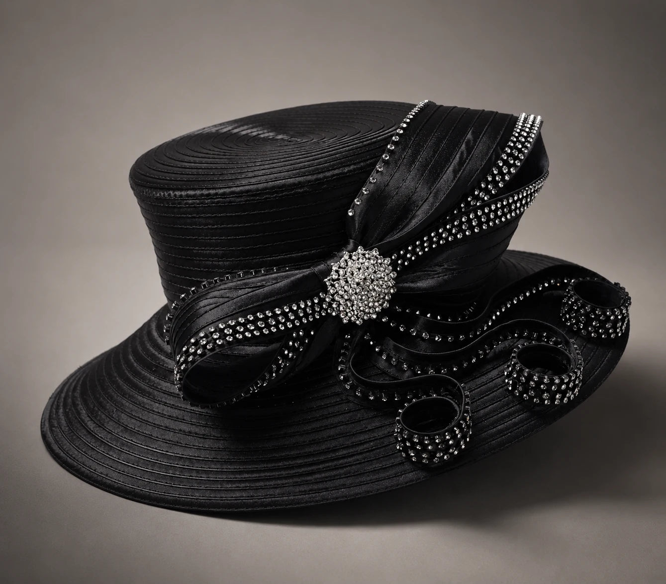 Black crystal embellished church hat with decorative ribbon loops and structured wide brim on neutral background