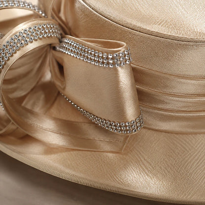 Close-up of champagne church hat featuring sparkling rhinestone ribbon trim and luxurious satin texture, premium women’s dress hat