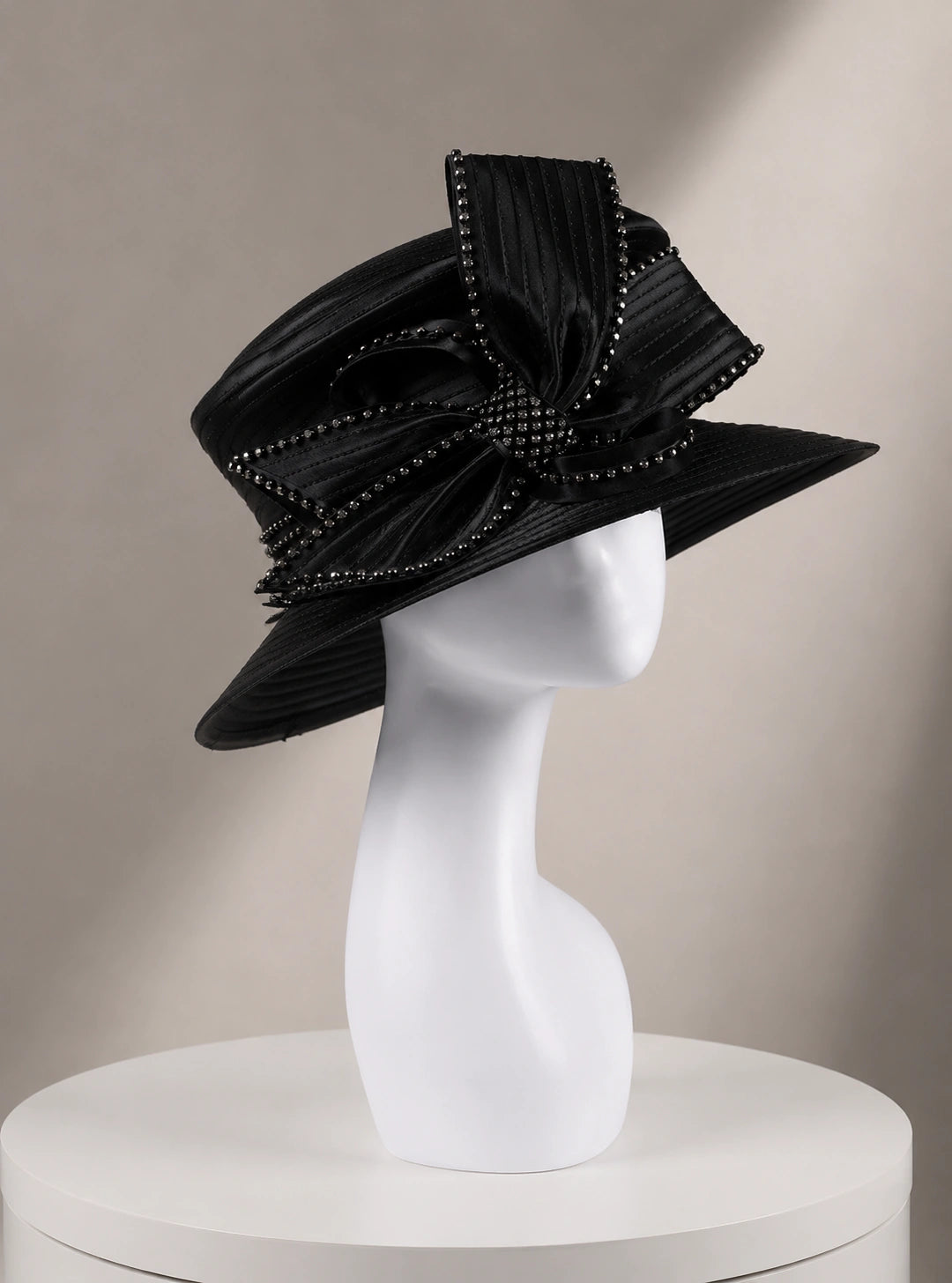Black church hat on mannequin, side angle view showing luxurious satin fabric and rhinestone bow details, ideal for formal events