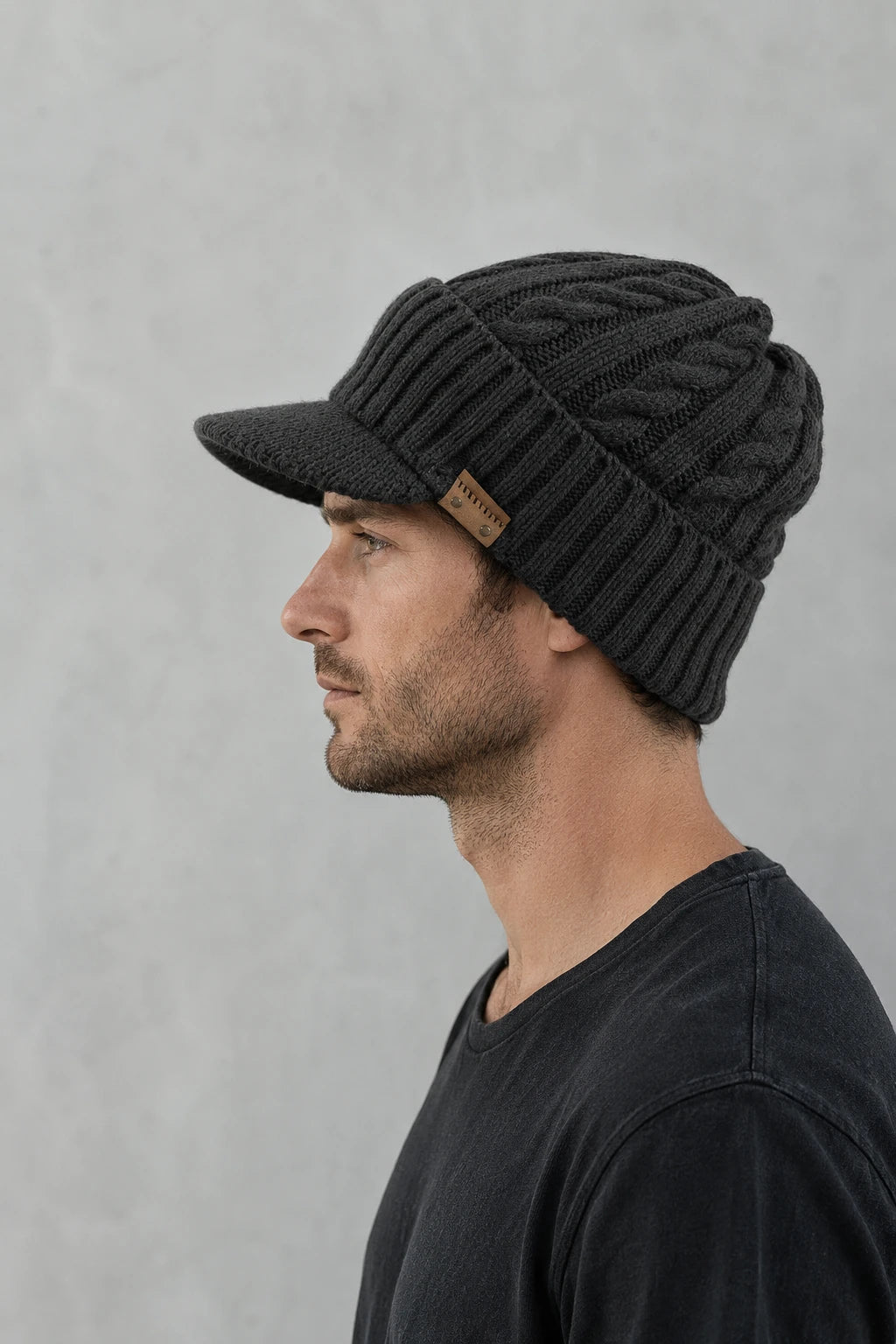 Side profile of a man wearing a dark gray cable knit visor beanie with a soft brim.