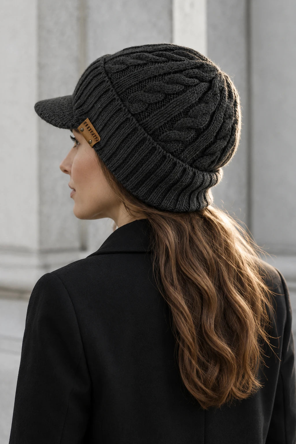 Side-back view of a woman wearing a dark gray cable knit visor beanie with her hair outside the hat.