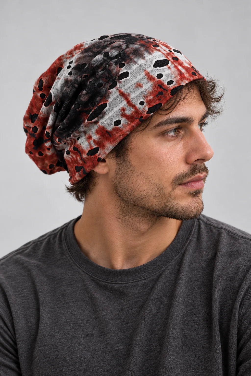 Man wearing the red, black and white B077 slouchy beanie, showing how it sits at the forehead and falls behind the head.