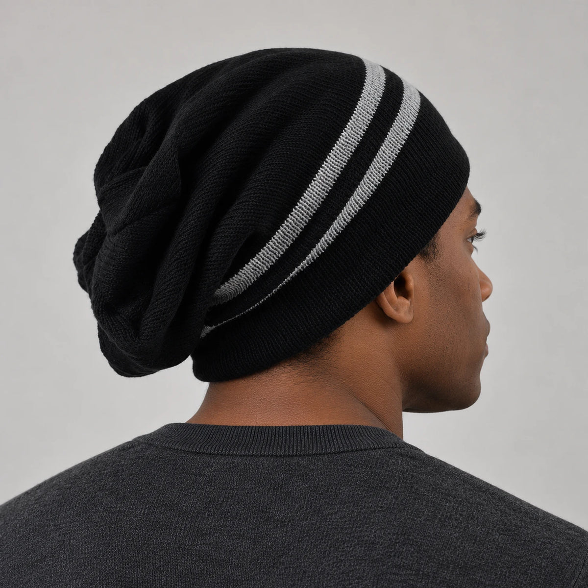 Side-back view of a man wearing the black striped B318 beanie, showing the draped crown.