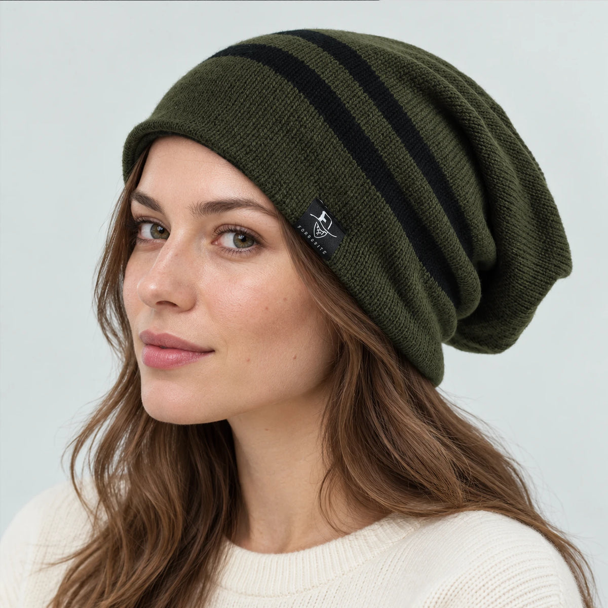 Woman wearing an olive green slouchy beanie with two black stripes and a draped back.
