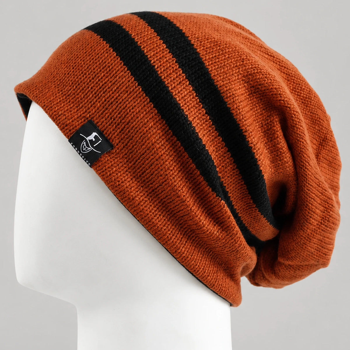 Rust orange slouchy beanie with two black stripes and a draped crown on a mannequin.