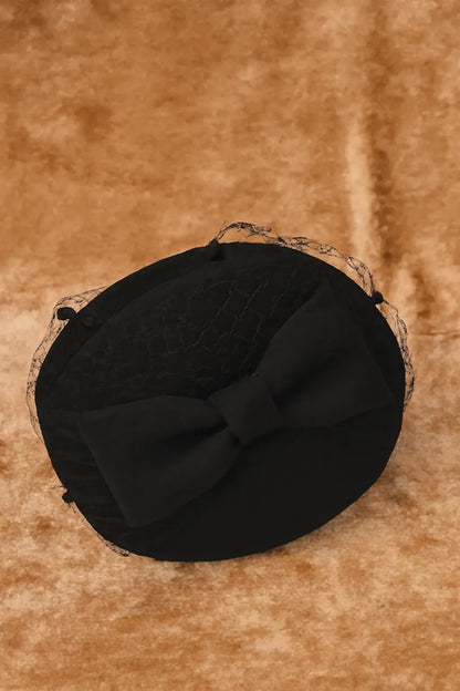 Elegant black pillbox fascinator hat with bow and birdcage veil on velvet background