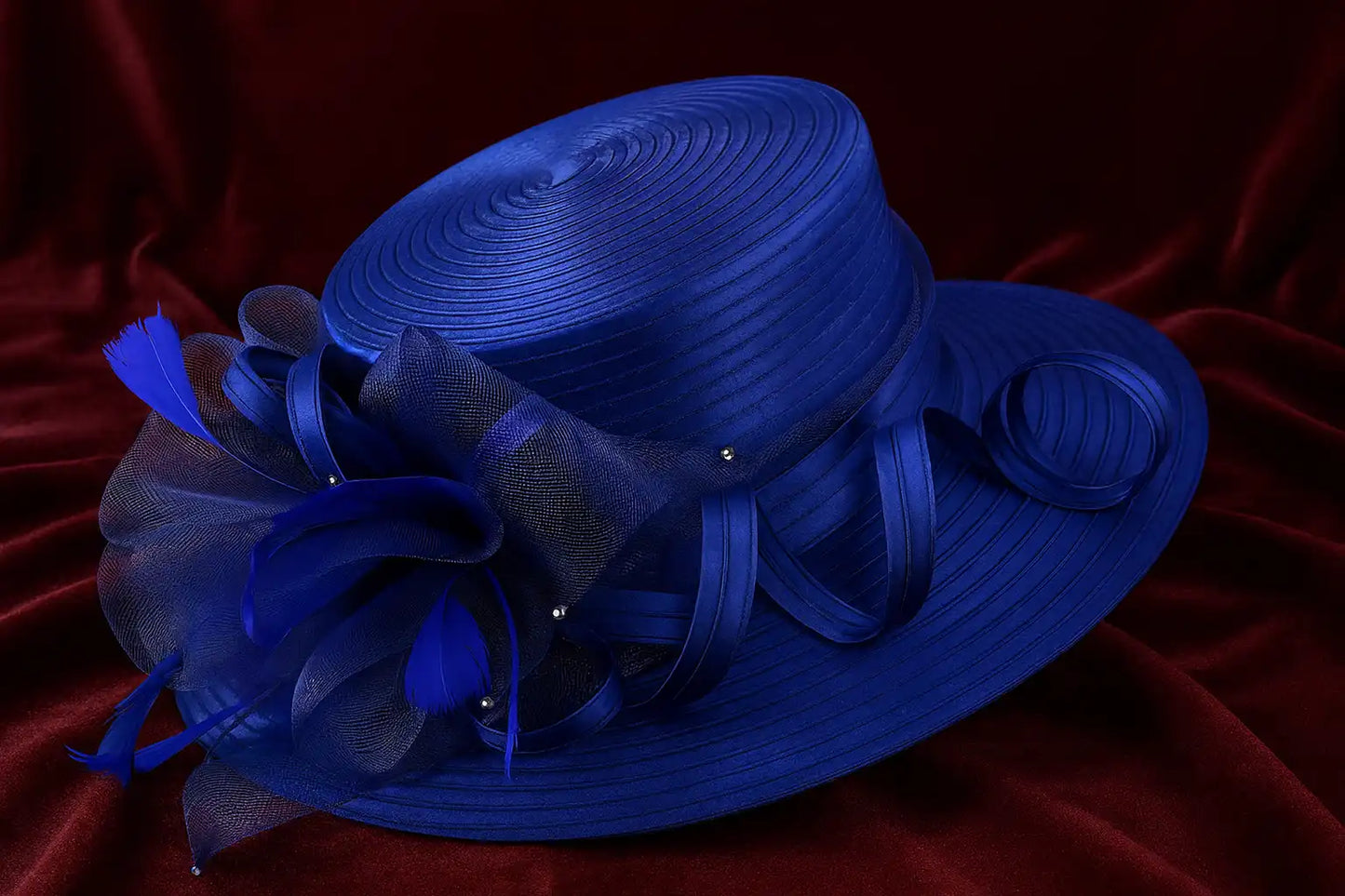 Statement royal blue church hat with satin spirals and feathers on burgundy velvet fabric – luxury occasion accessory