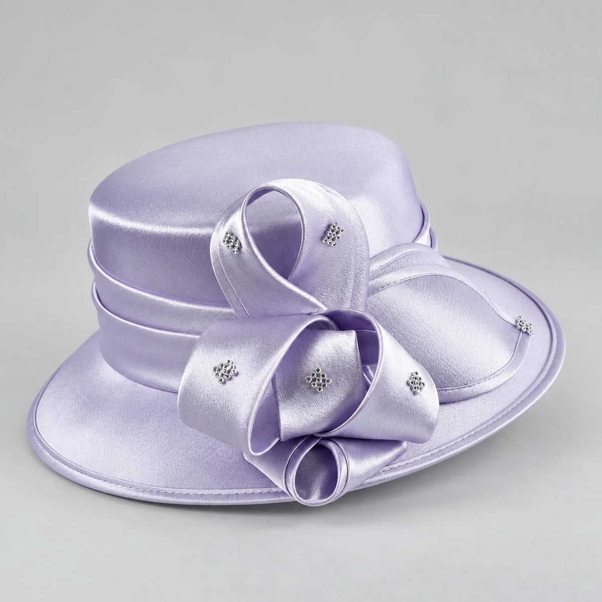 Angled view of a lavender church hat showing its layered satin bow, rounded crown and rhinestone details