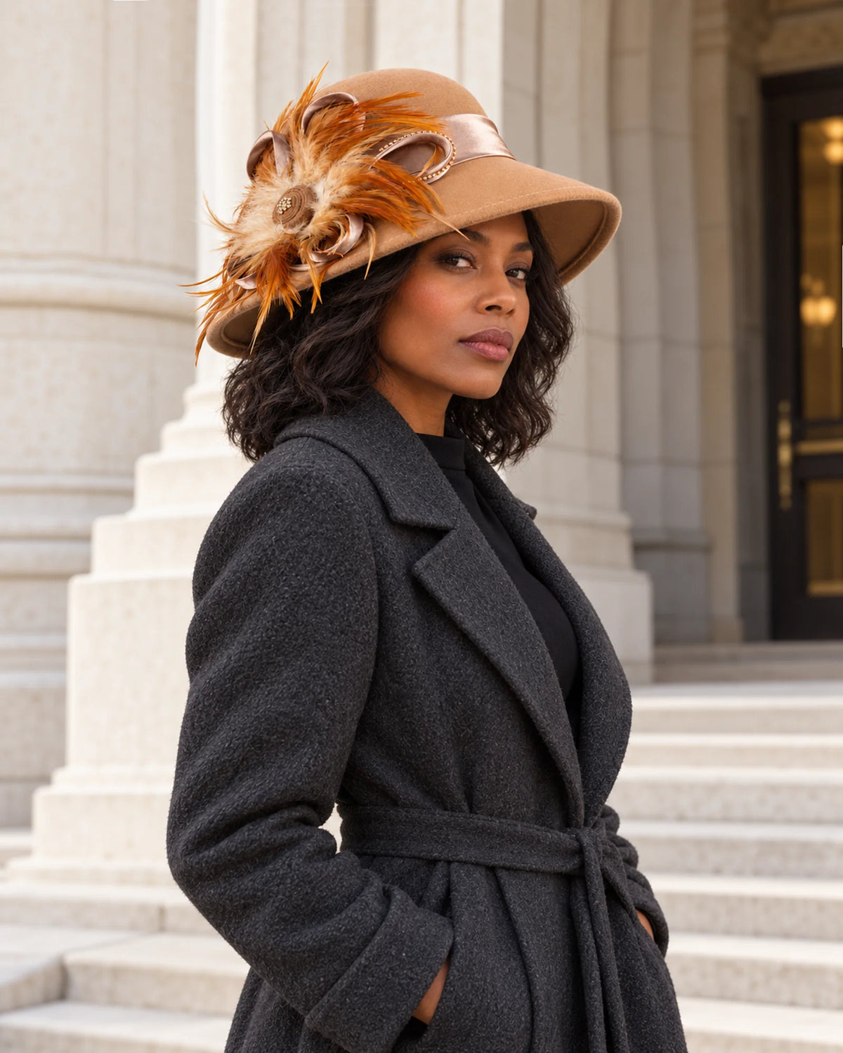 Woman wearing the camel feather-trimmed wool hat with a dark coat outside a stone building