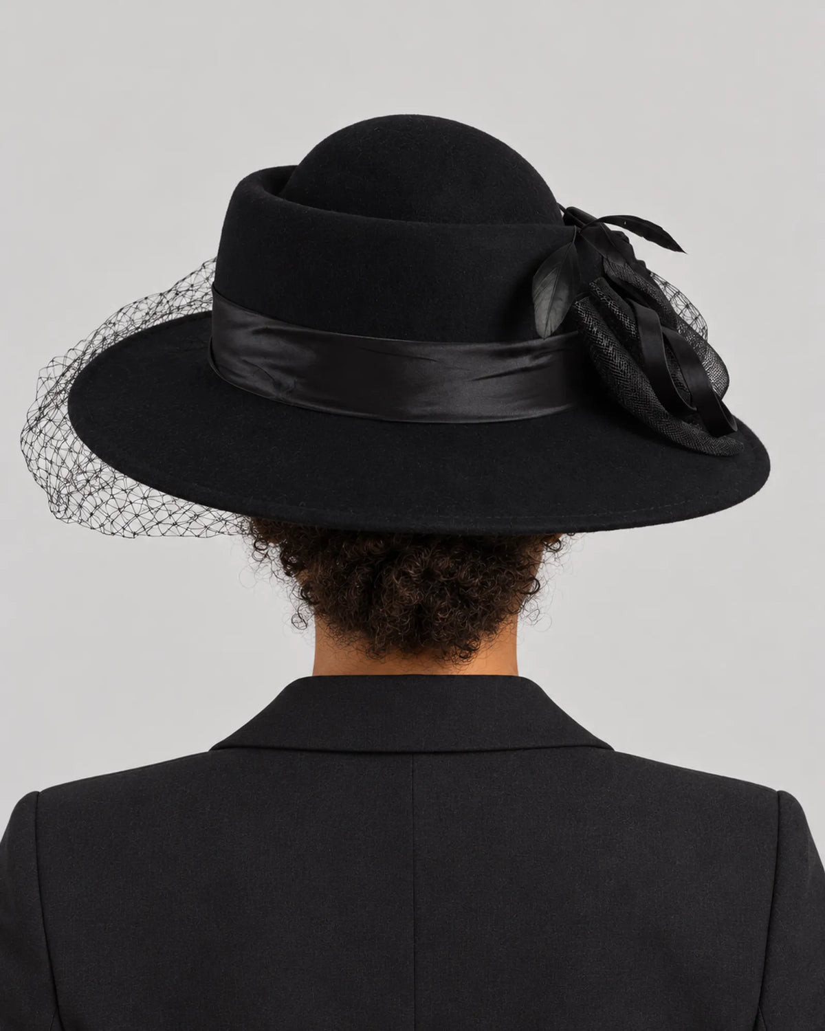Rear view of the black Z029B hat on a woman, showing its rounded crown and veil behind the brim.