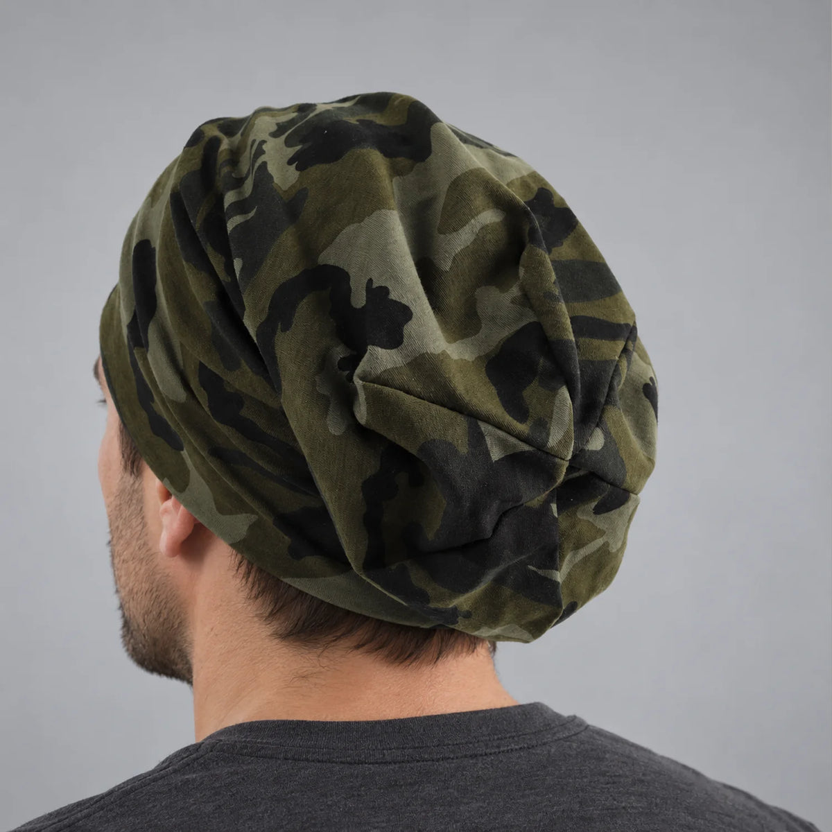 Rear view of a man wearing a forest green camo slouchy beanie with relaxed back drape
