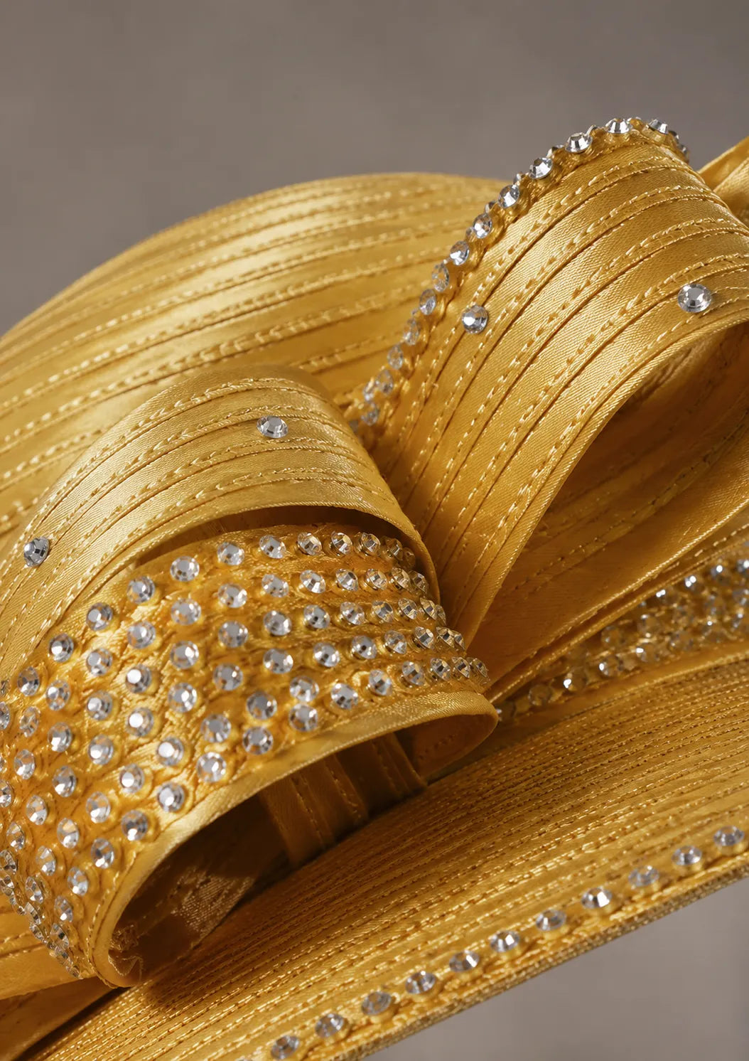 Close-up detail of a gold church hat featuring sparkling rhinestones, satin ribbon loops and luxury decorative trim craftsmanship.