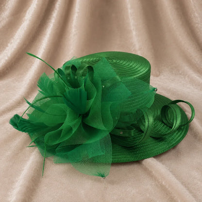 Emerald green satin church hat with feather accents and decorative mesh flower displayed on fabric background, sophisticated women’s dress hat