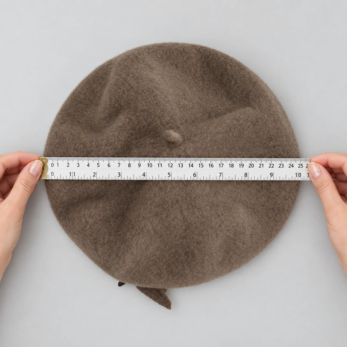 Hands holding a ruler across the taupe beret while it lies flat