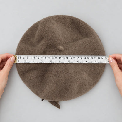 Hands holding a ruler across the taupe beret while it lies flat