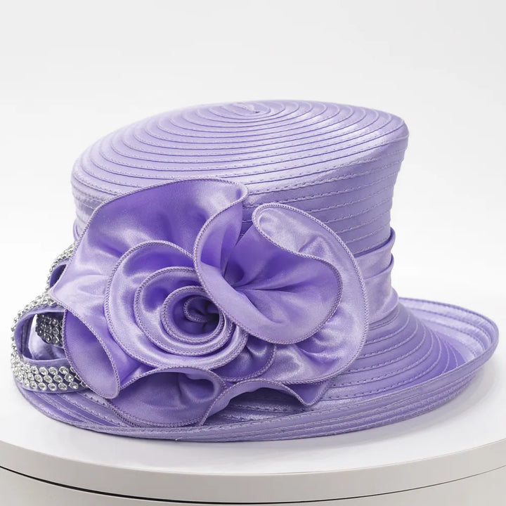 Front view of a lavender satin church hat with a large rose appliqué and rhinestone trim on a white display stand.