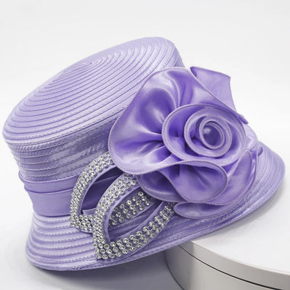 Side view of a lavender church hat featuring satin floral detailing and double-loop rhinestone accents, displayed on a white stand.