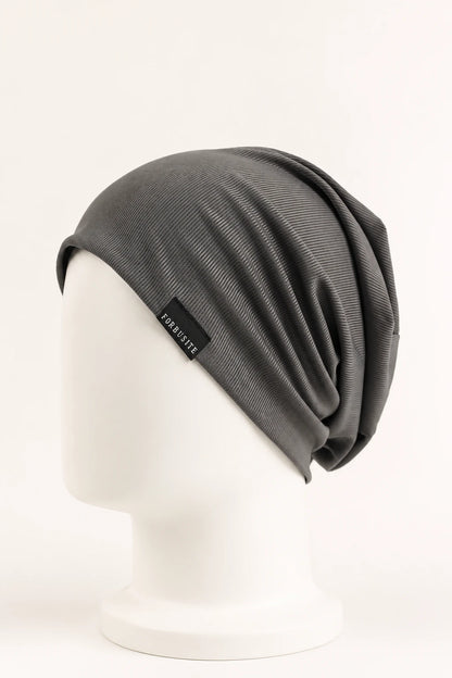 A dark gray slouchy knit beanie hat displayed on a white mannequin head against a clean white background. A small black brand tag on the side reads 'KABUSHIT'.