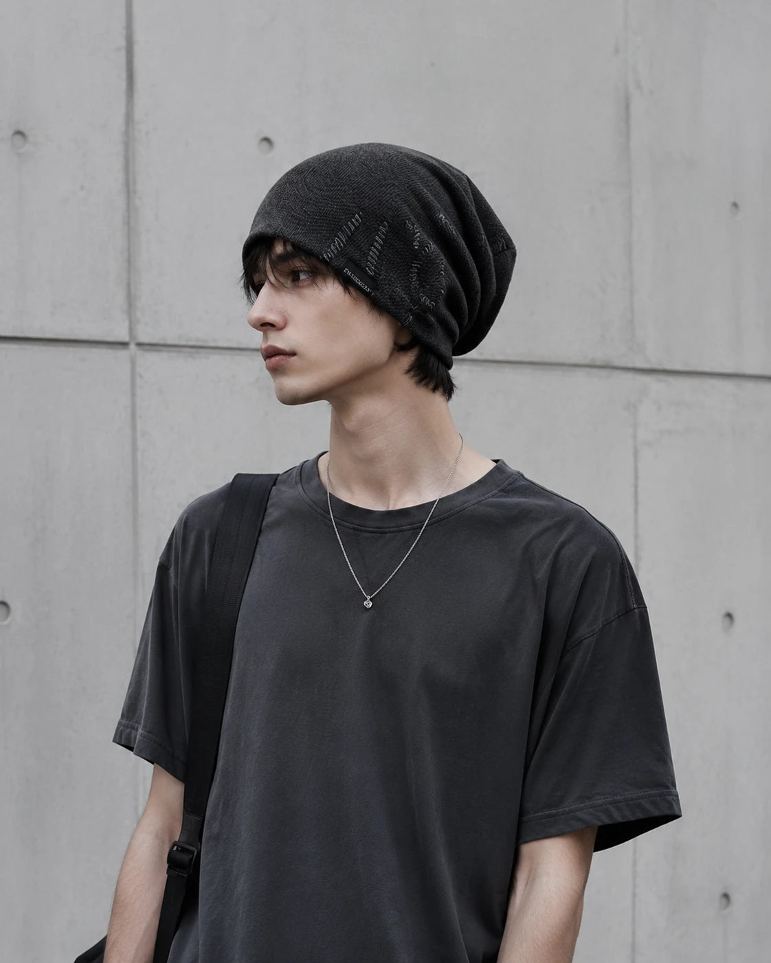 Young man wearing a charcoal black slouchy beanie in minimalist urban streetwear style with relaxed oversized fit
