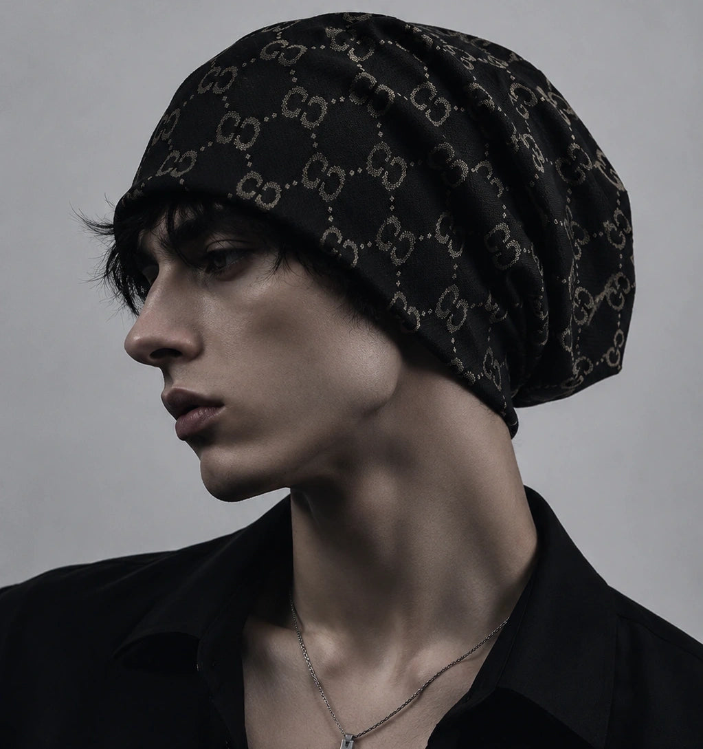 Male model wearing a black oversized slouchy beanie cap with vintage jacquard double C pattern, soft knit fabric, modern streetwear style.