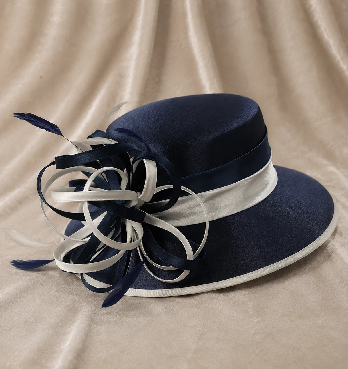 Navy blue satin church hat with white ribbon details and feather accents displayed on soft fabric background, elegant women’s dress hat