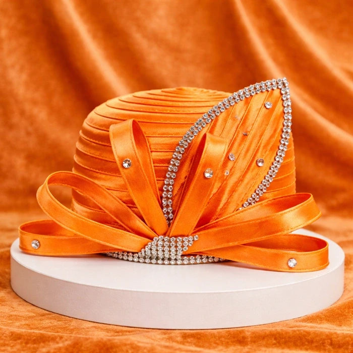 Vibrant orange satin church hat with rhinestone accents and satin ribbon detailing, showcased on a white base with an orange velvet background.