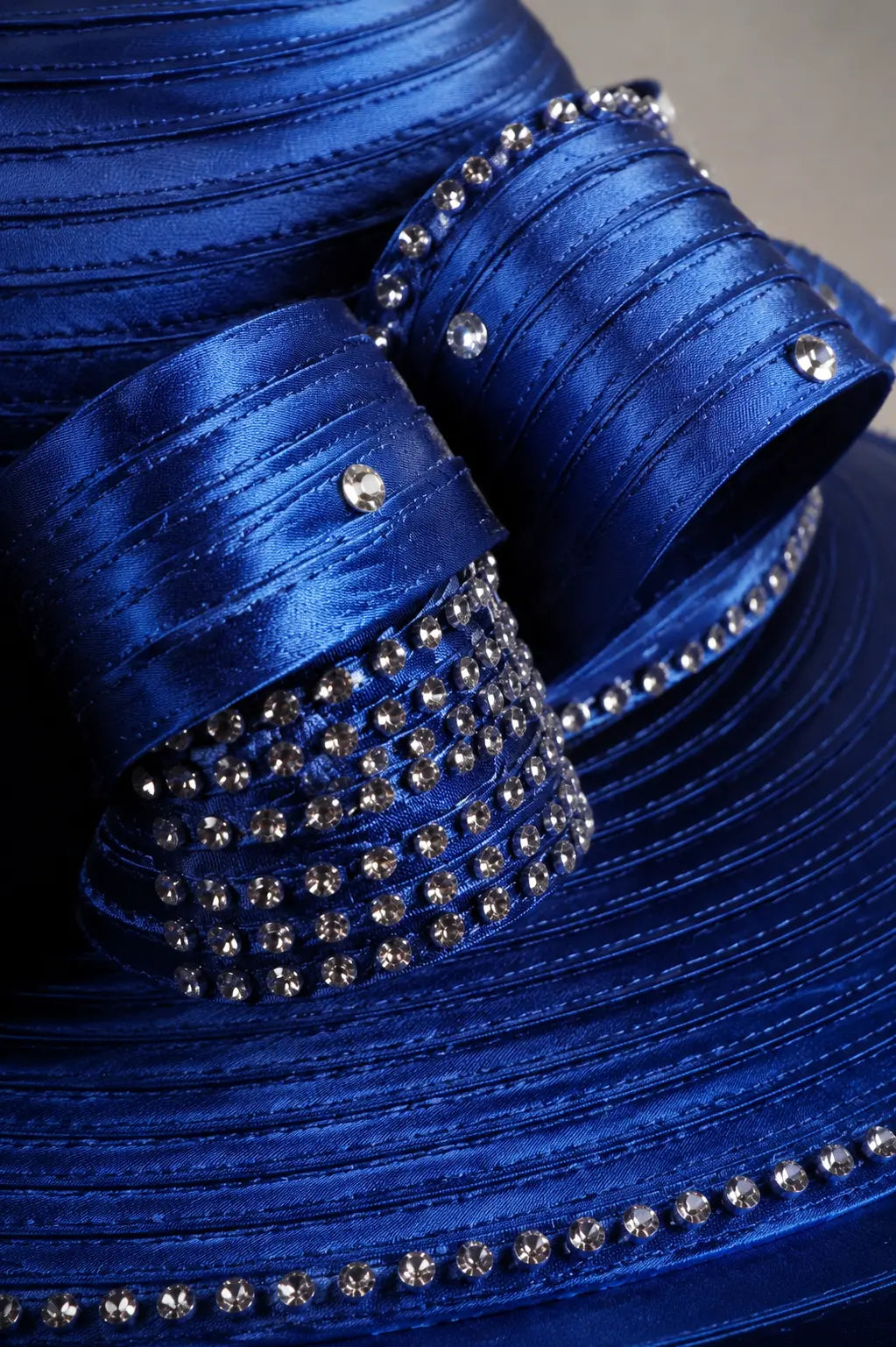 Close-up detail of a royal blue church hat showing rhinestone embellishments, satin ribbon loops and premium craftsmanship.