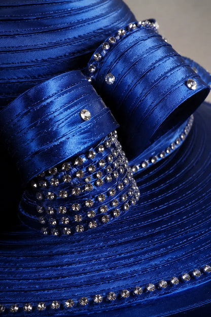 Close-up detail of a royal blue church hat showing rhinestone embellishments, satin ribbon loops and premium craftsmanship.