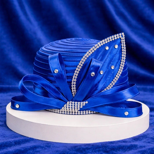 Royal blue satin church hat with layered satin ribbons and rhinestone embellishments, elegantly displayed against a rich blue velvet background.