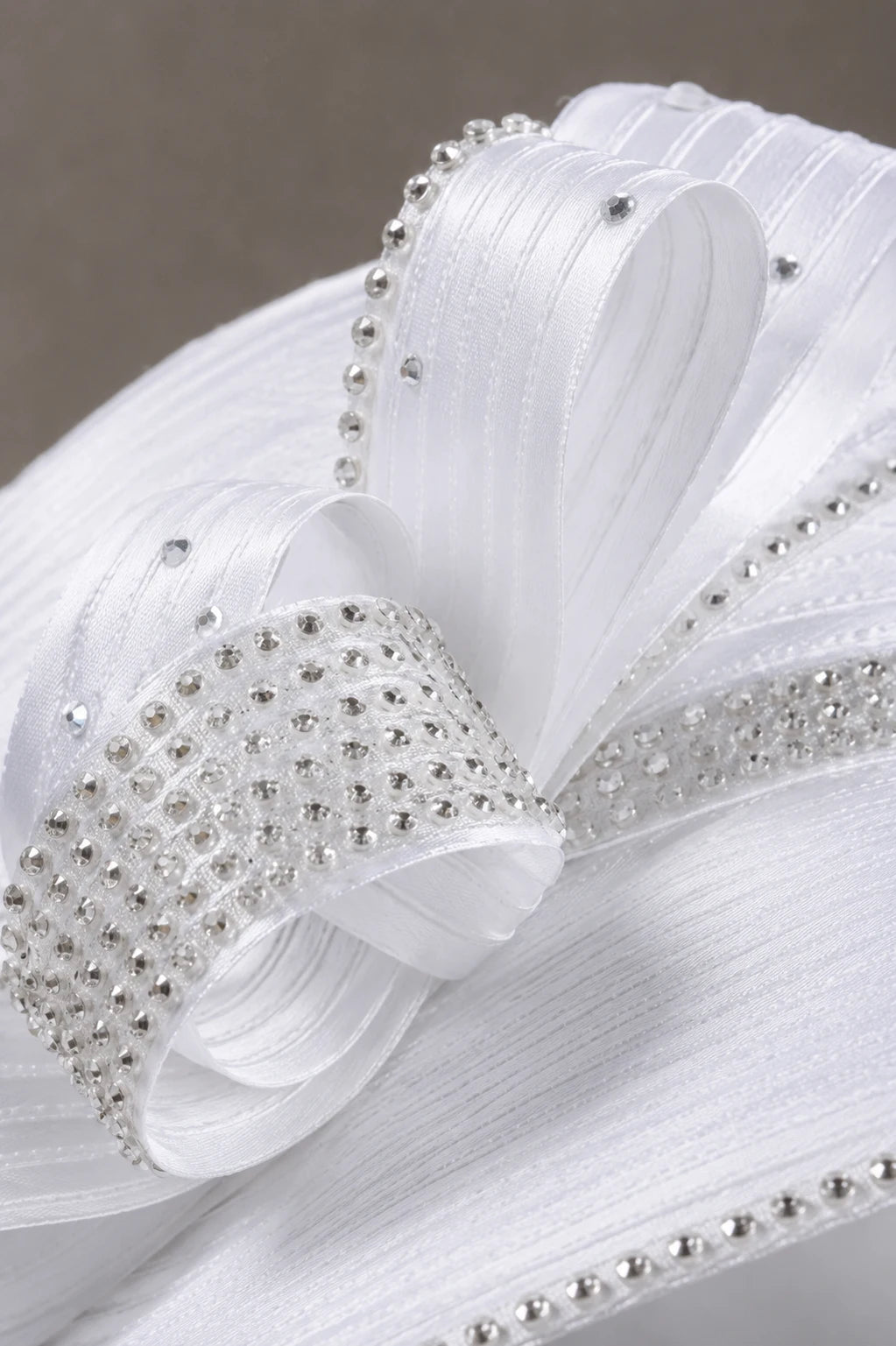Close up detail of white church hat featuring rhinestone embellishments, decorative ribbon loops and premium craftsmanship