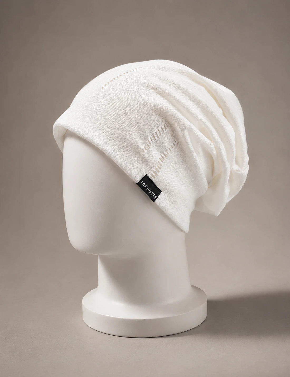 White slouchy knit beanie in minimalist style displayed on mannequin with soft neutral luxury background