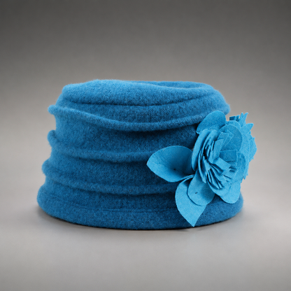 A bright blue felt hat with a large matching felt flower accent on the side, photographed against a neutral gray gradient background.