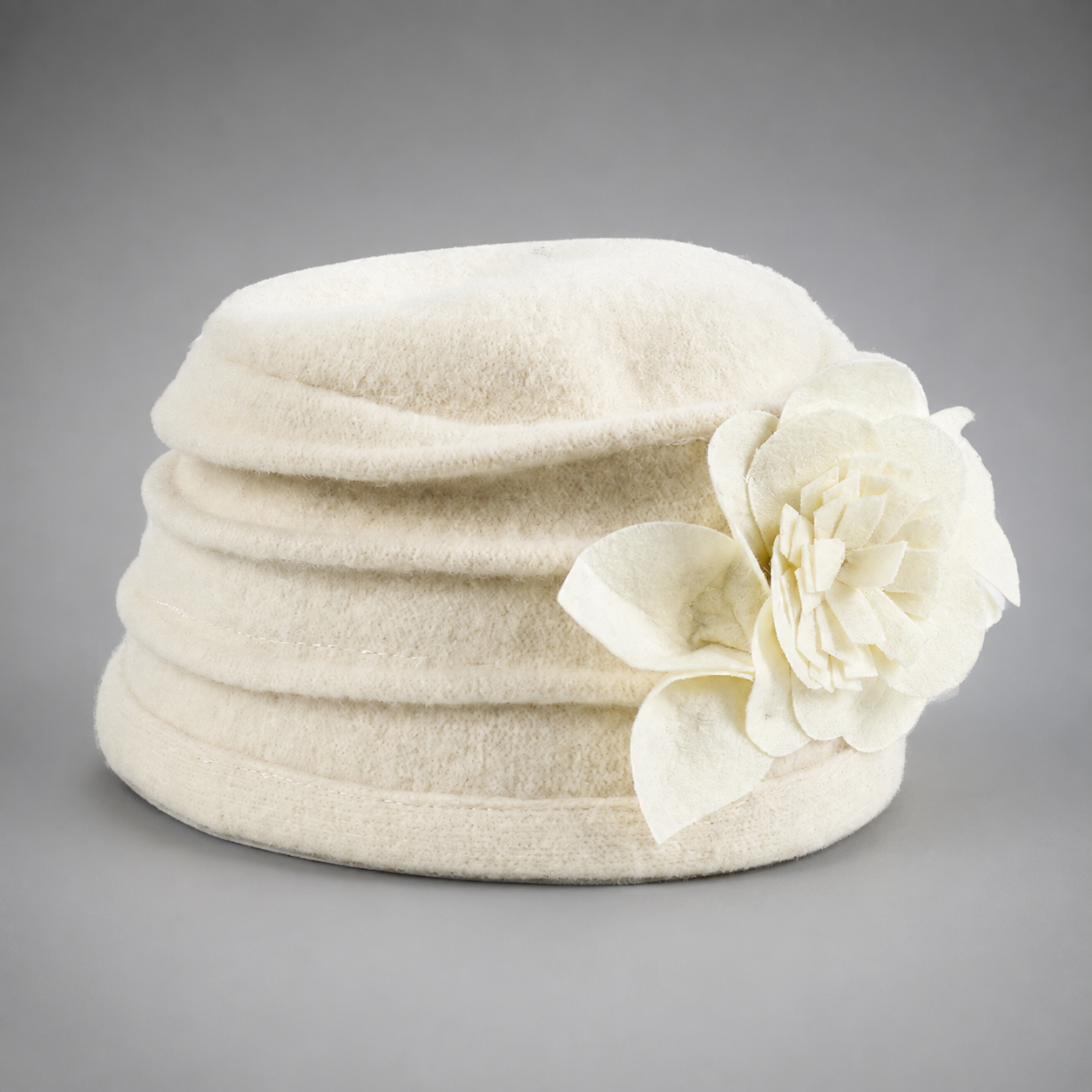 An off-white felt hat with a large matching fabric flower accent on the side, photographed against a neutral gray background.
