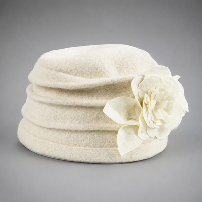An off-white felt hat with a large matching fabric flower accent on the side, photographed against a neutral gray background.