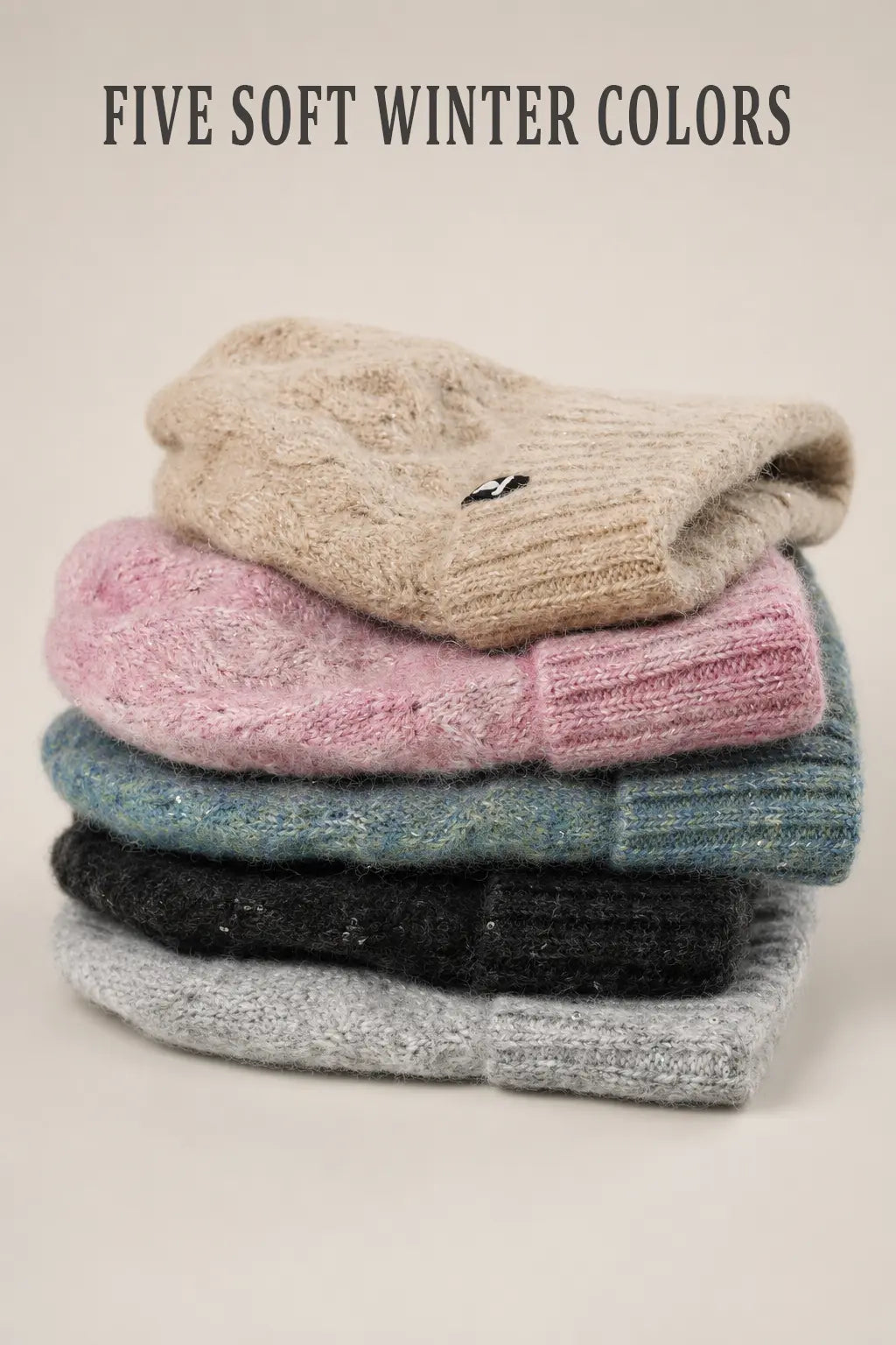 Five fuzzy cuffed winter beanies stacked in beige, pink, light blue, black and light gray.