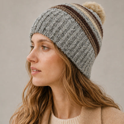 Woman wearing a gray striped knit beanie with a fixed faux fur pom pom