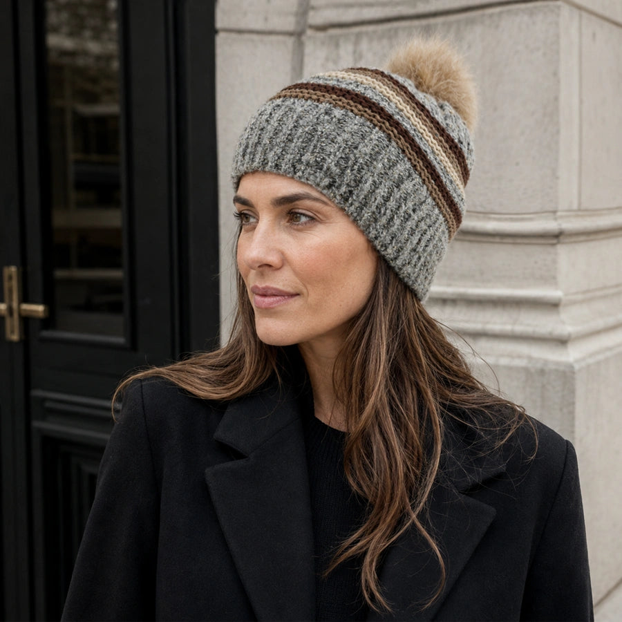 Women’s gray striped pom pom beanie styled with a black coat outdoors