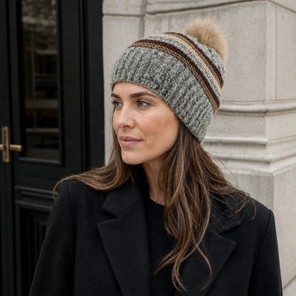 Women’s gray striped pom pom beanie styled with a black coat outdoors