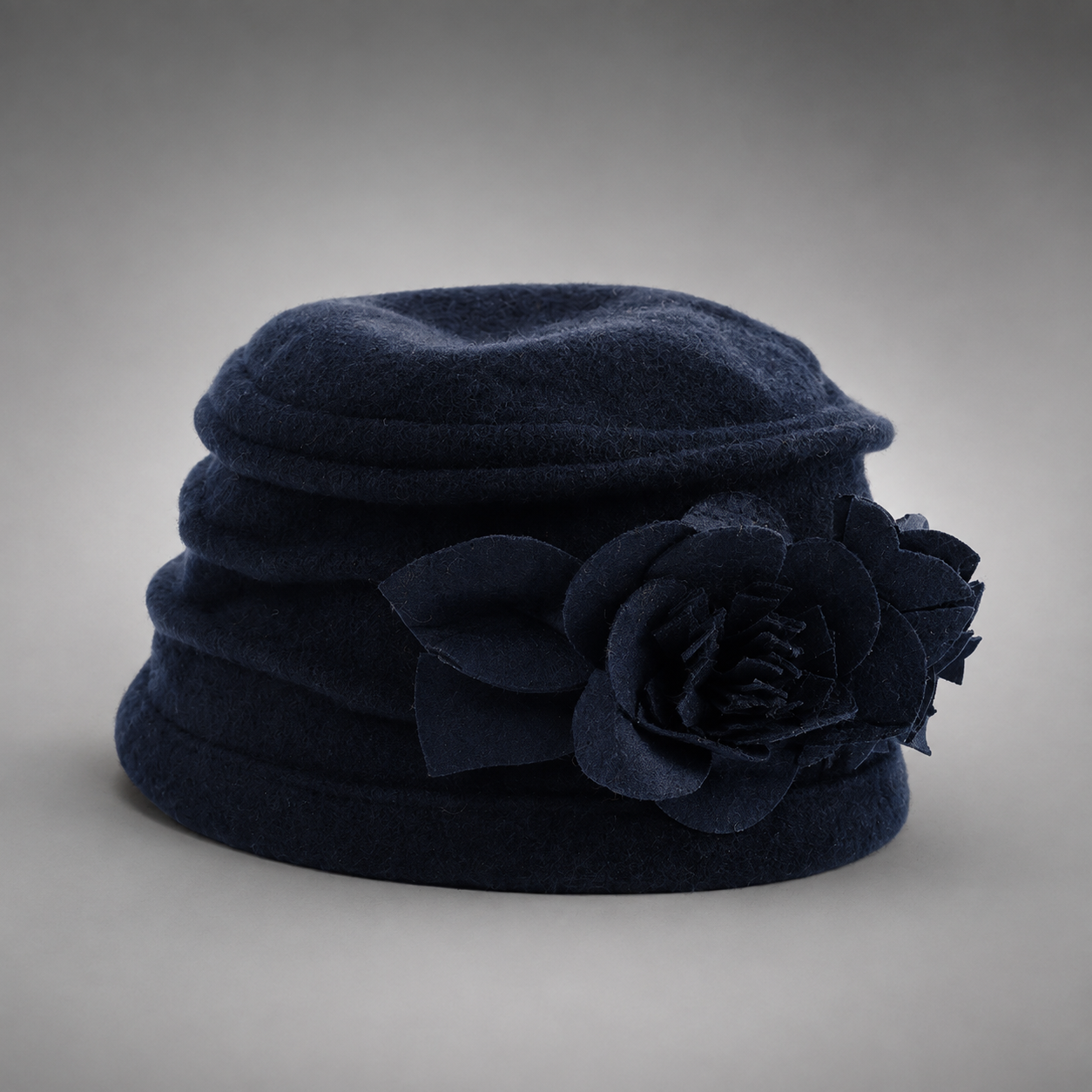 A dark navy blue felt hat featuring a large matching fabric flower decoration on the side, photographed against a neutral gray gradient background.