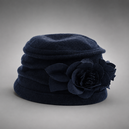 A dark navy blue felt hat featuring a large matching fabric flower decoration on the side, photographed against a neutral gray gradient background.
