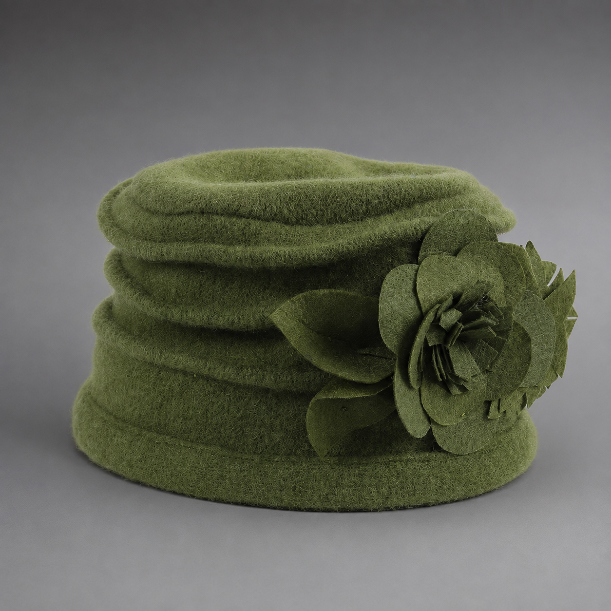 An olive green felt hat with a large matching felt flower decoration on the side, photographed against a neutral gray background.