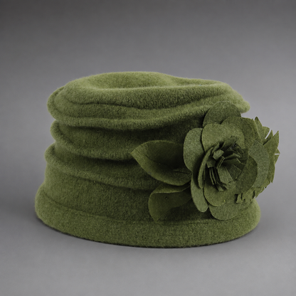 An olive green felt hat with a large matching felt flower decoration on the side, photographed against a neutral gray background.