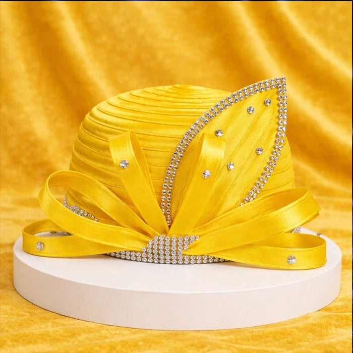 Bright yellow satin church hat with rhinestone accents, beautifully arranged on a simple white platform against a yellow velvet backdrop.